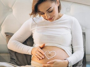 Вагітна жінка малює серце на животі кремом Вагітна жінка малює серце на животі кремом
