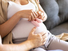 Вагітна жінка тримає рожеві пінетки на животі Вагітна жінка тримає рожеві пінетки на животі